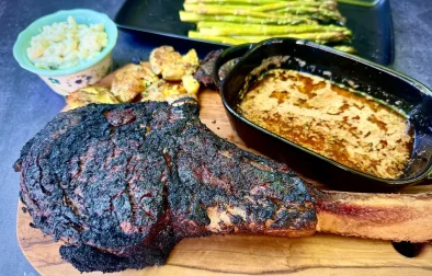 whole tomahawk steak grilled on cutting board with cowboy butter, potatoes, and asparagus